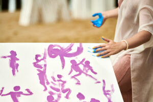 Woman hand smearing blue paint on canvas, art expression at outdoor art festival, art improvisation
