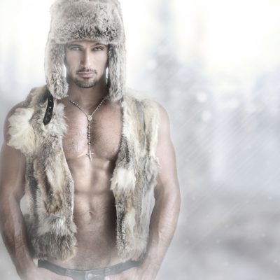 Fashion portrait of a beautiful male model in fur hat and vest against modern background with copy space